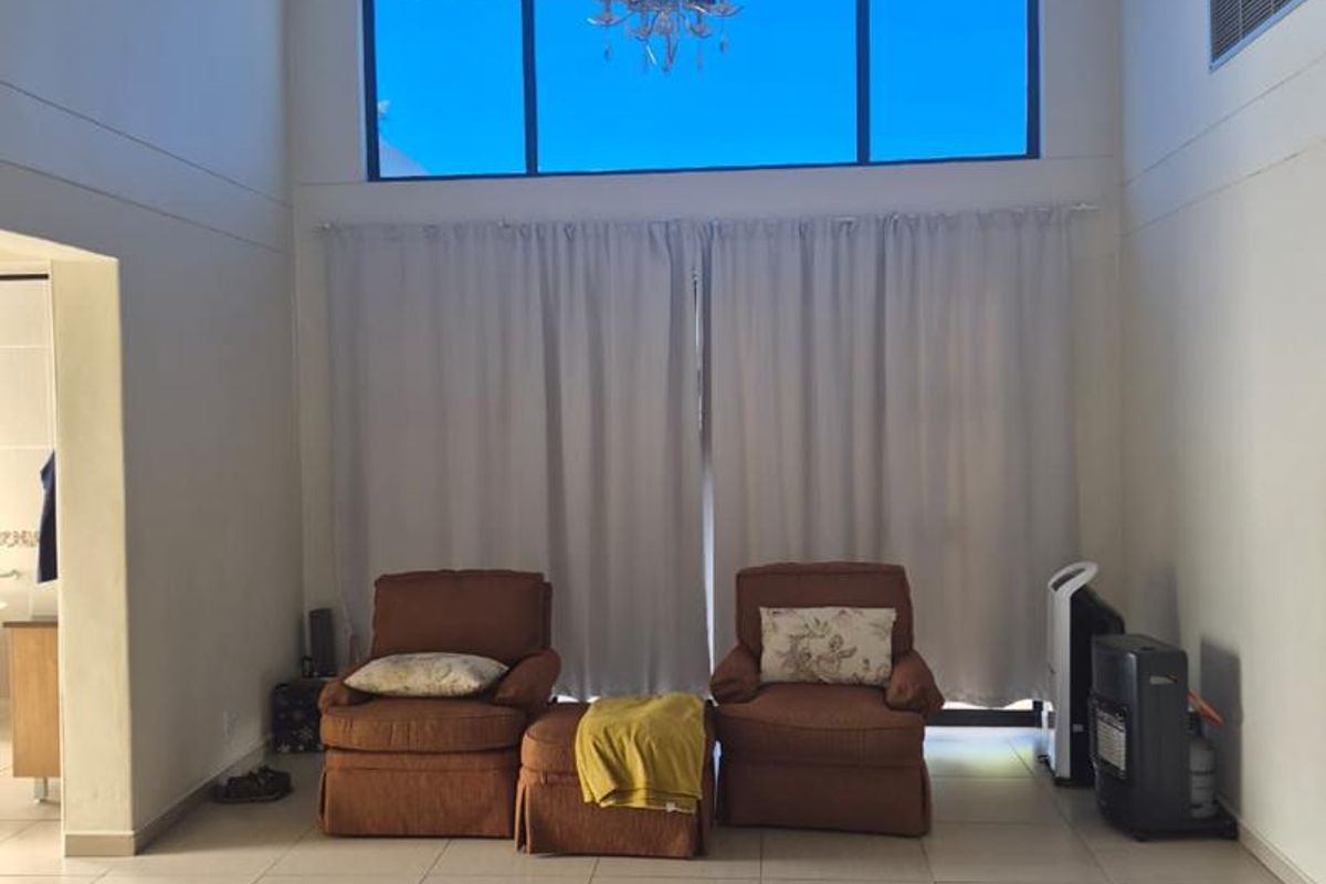 Spacious bedroom featuring high vaulted ceilings with exposed trusses, large floor-to-ceiling windows, and neutral tiled flooring.