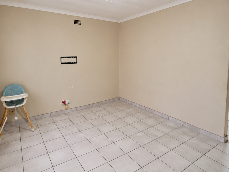 A neutral-toned living area featuring tiled flooring, an arched entryway, and a wall-mounted TV bracket, offering a clean and versatile space.