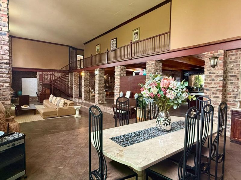 Spacious open-plan living and dining area featuring exposed brick columns, a wooden staircase, and a mezzanine level with a balcony railing.