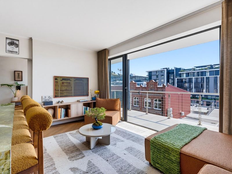 Bright living room featuring parquet flooring and large sliding glass doors that open onto a private balcony with urban views.
