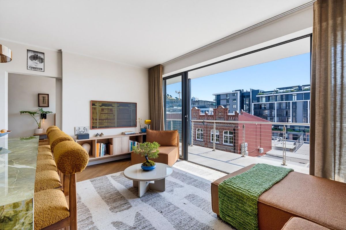 Bright living room featuring parquet flooring and large sliding glass doors that open onto a private balcony with urban views.