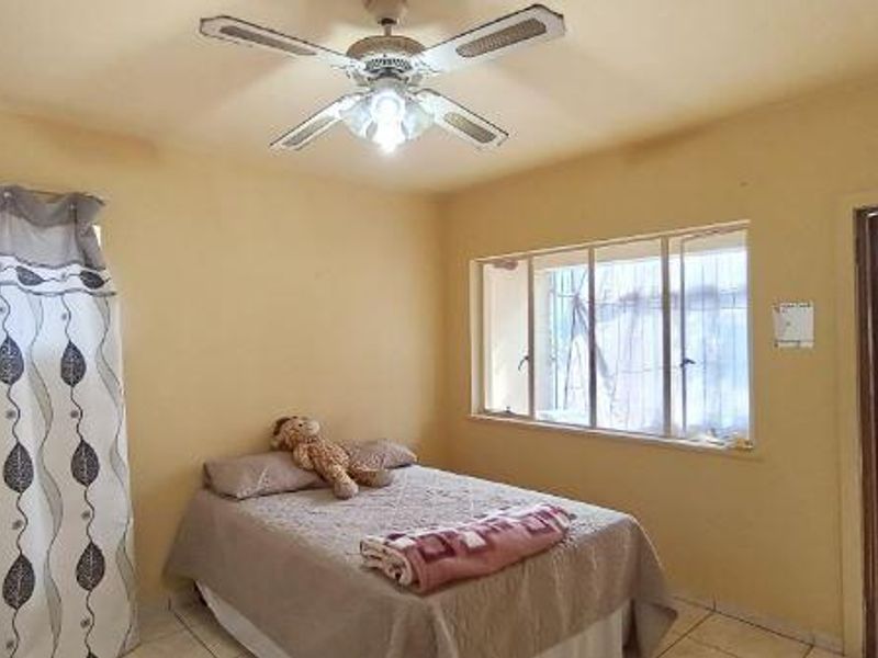 A bedroom featuring tiled flooring, a ceiling fan, and a window with security bars, requiring cosmetic updates to improve its overall appeal.