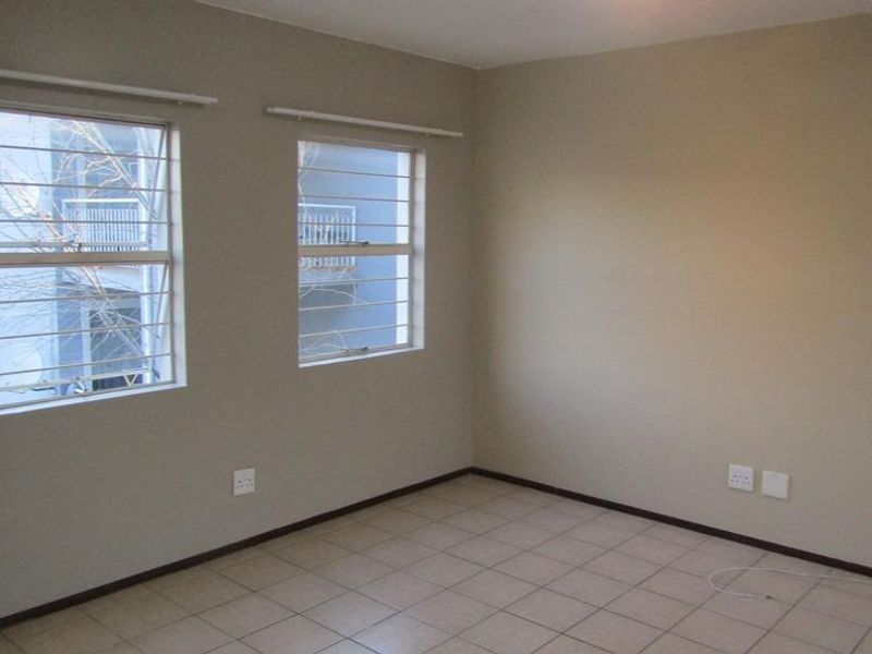 An empty bedroom featuring neutral wall paint, tiled flooring, and windows fitted with security bars.
