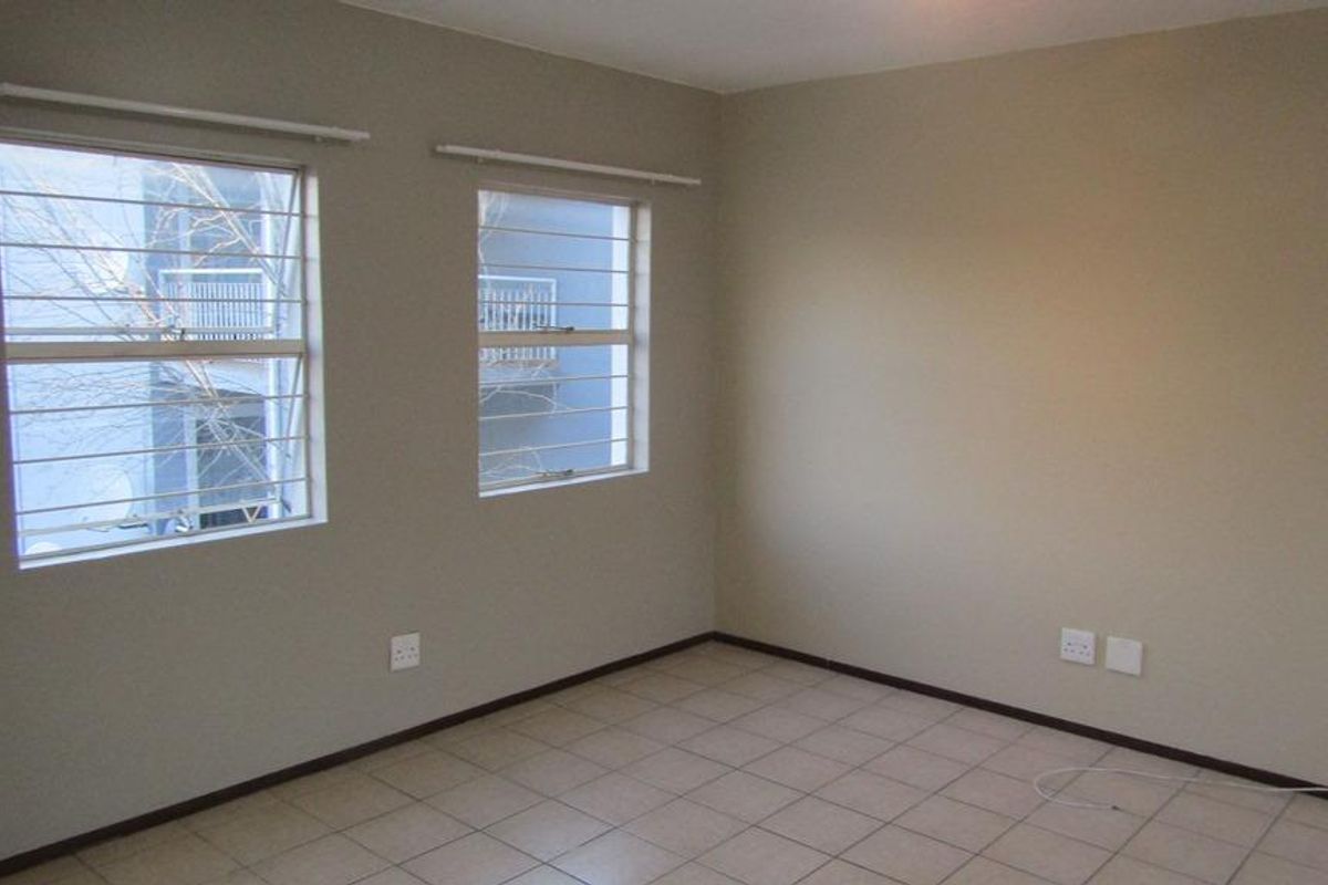 An empty bedroom featuring neutral wall paint, tiled flooring, and windows fitted with security bars.