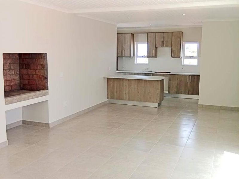 Spacious open-plan living area featuring a built-in brick fireplace and a modern kitchen with wood-finish cabinetry and a central island.