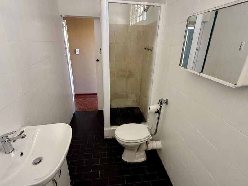 A functional bathroom featuring a shower enclosure, toilet, and pedestal basin with white wall tiling and dark floor tiles.