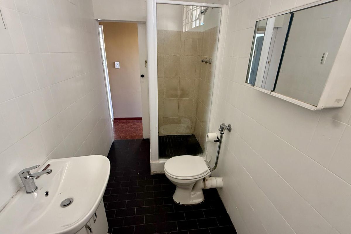 A functional bathroom featuring a shower enclosure, toilet, and pedestal basin with white wall tiling and dark floor tiles.