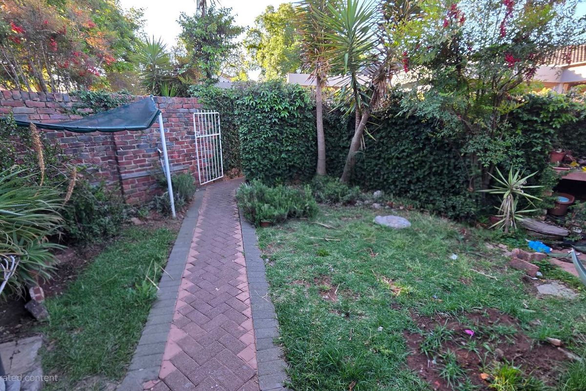 A private rear garden featuring a brick-paved pathway, established perimeter brick walls, and mature landscaping, offering a secluded outdoor space.