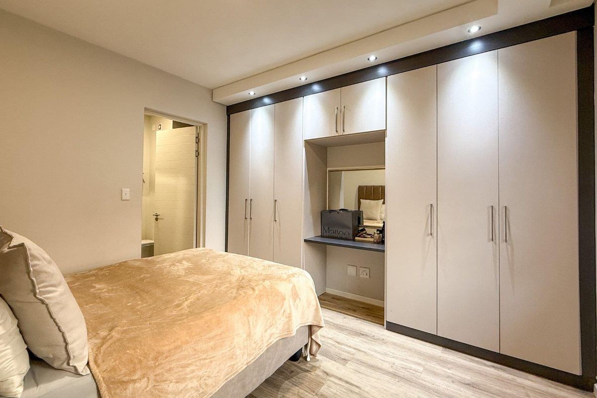Modern bedroom featuring extensive built-in cabinetry with an integrated vanity nook, recessed ceiling lighting, and durable laminate flooring, with direct access to an en-suite bathroom.