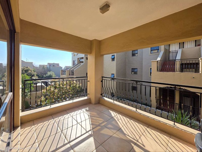 A covered balcony featuring tiled flooring and a decorative wrought iron balustrade, offering an open view of the surrounding apartment complex.