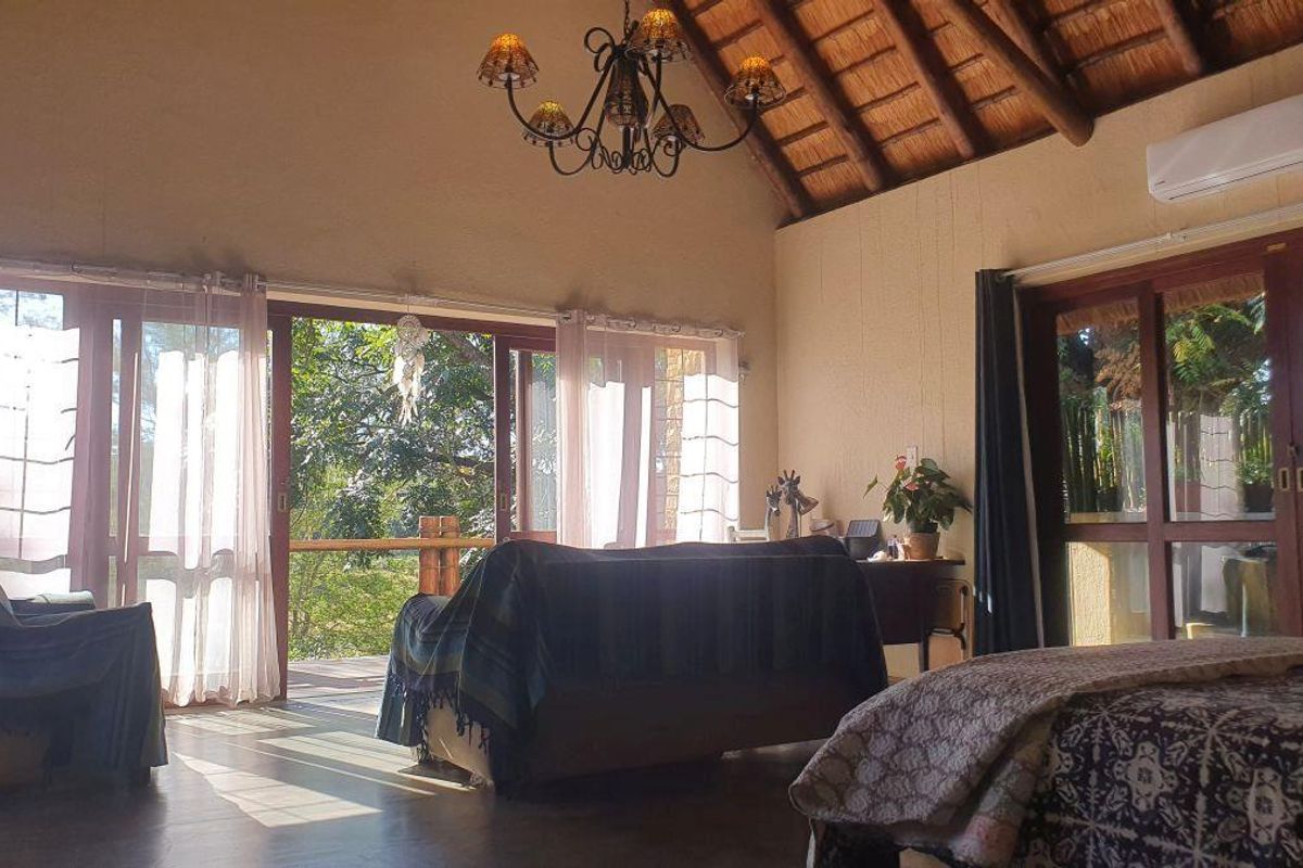 Spacious living area featuring a high thatched ceiling, exposed timber beams, and large glass sliding doors opening onto a private outdoor deck.