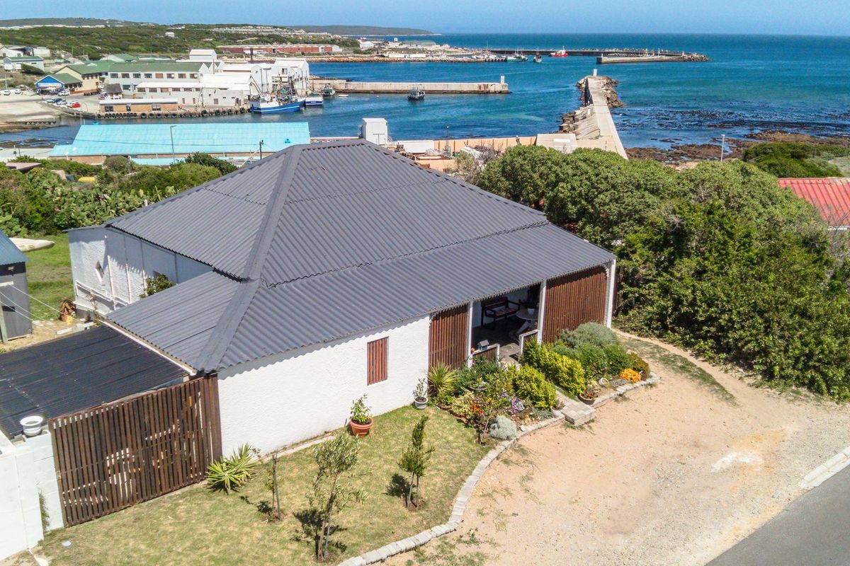 Aerial view of a coastal property featuring a dark metal roof, white exterior walls, and a covered patio area overlooking the harbour.