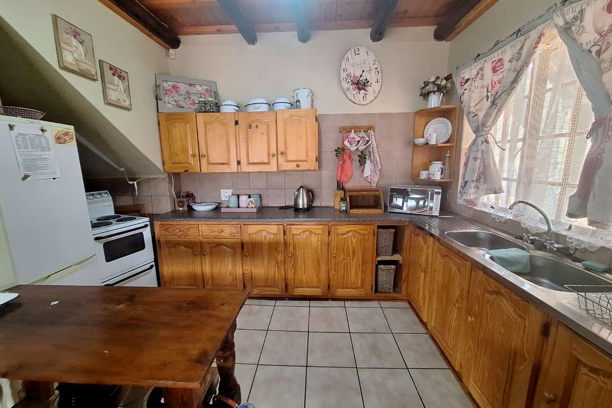 A rustic kitchen featuring wooden cabinetry, tiled countertops, a double sink, and exposed timber ceiling beams.