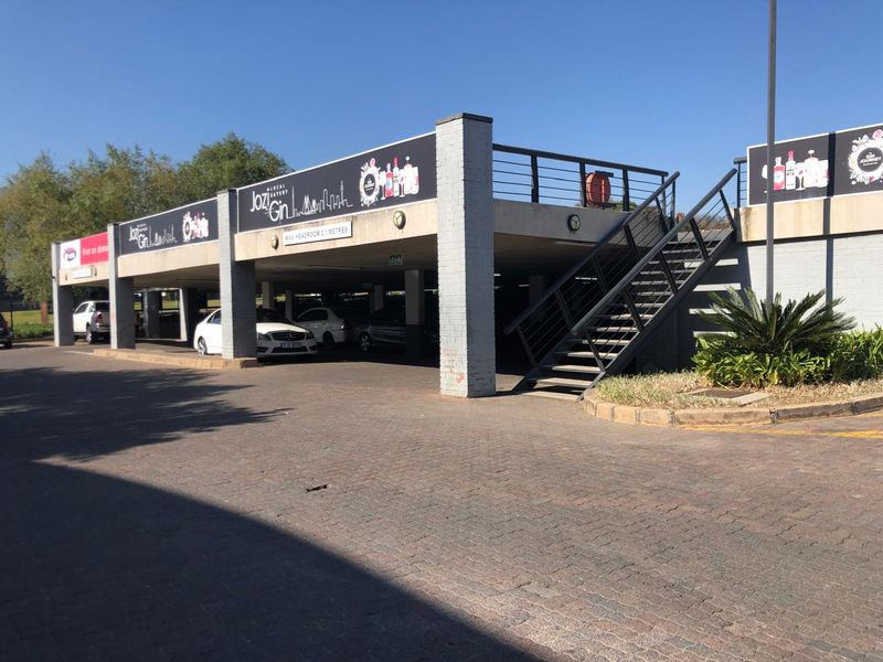 Exterior view of a commercial property featuring a covered parking area with concrete pillars and an external metal staircase leading to an upper level.