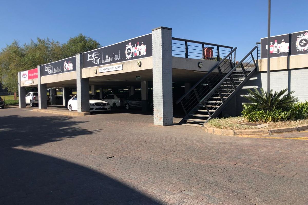 Exterior view of a commercial property featuring a covered parking area with concrete pillars and an external metal staircase leading to an upper level.