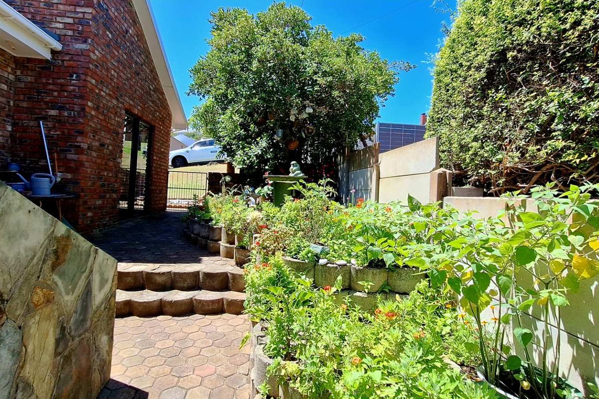 A paved rear garden area featuring tiered stone retaining walls, established garden beds, and brick exterior walling.