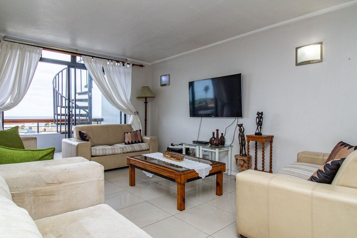 A comfortable living room featuring tiled flooring, wall-mounted lighting, and large sliding glass doors that open onto a balcony with a spiral staircase.