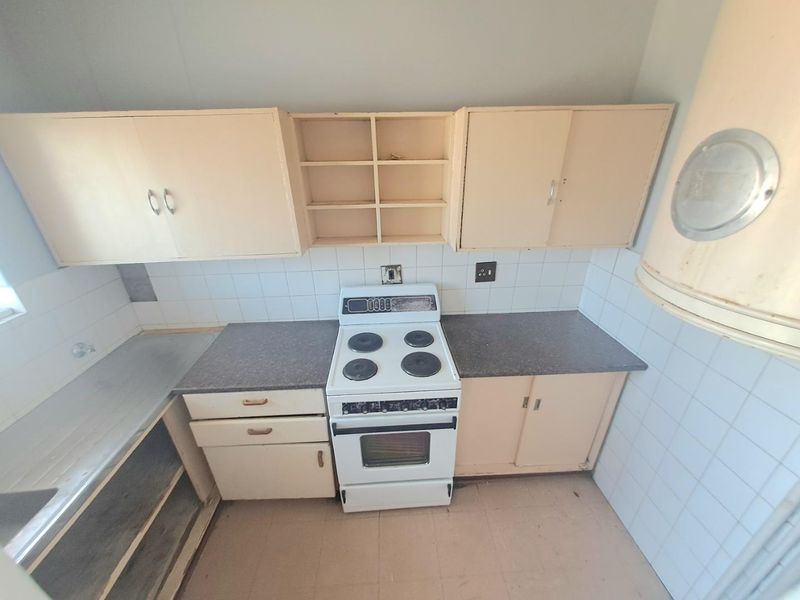 A dated kitchen featuring original cabinetry, laminate countertops, a tiled backsplash, and a freestanding electric stove, offering significant potential for modernization.
