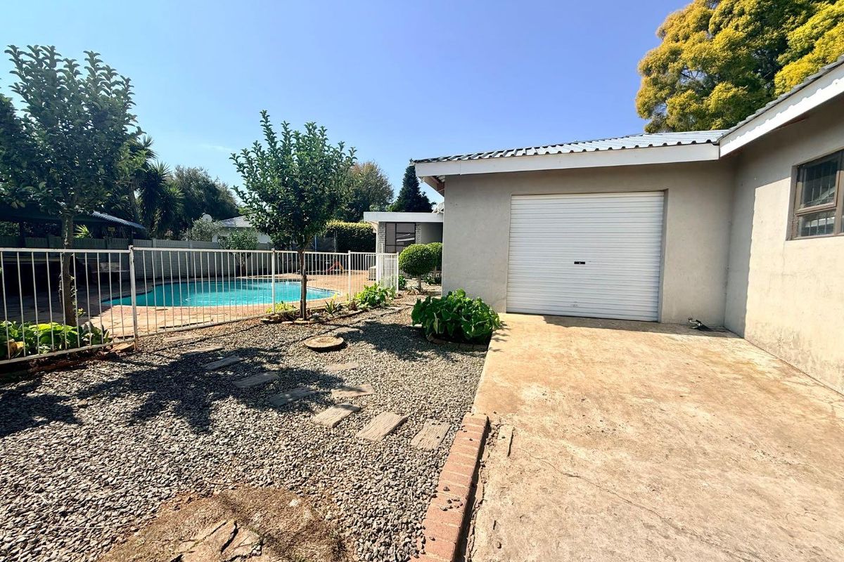 Rear exterior view featuring a concrete driveway, a single garage with a roller door, and a fenced swimming pool area.
