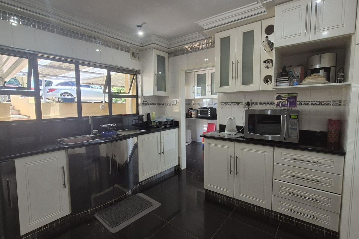 A functional kitchen featuring white cabinetry, black granite countertops, dark floor tiles, and a double sink with a view of the exterior.