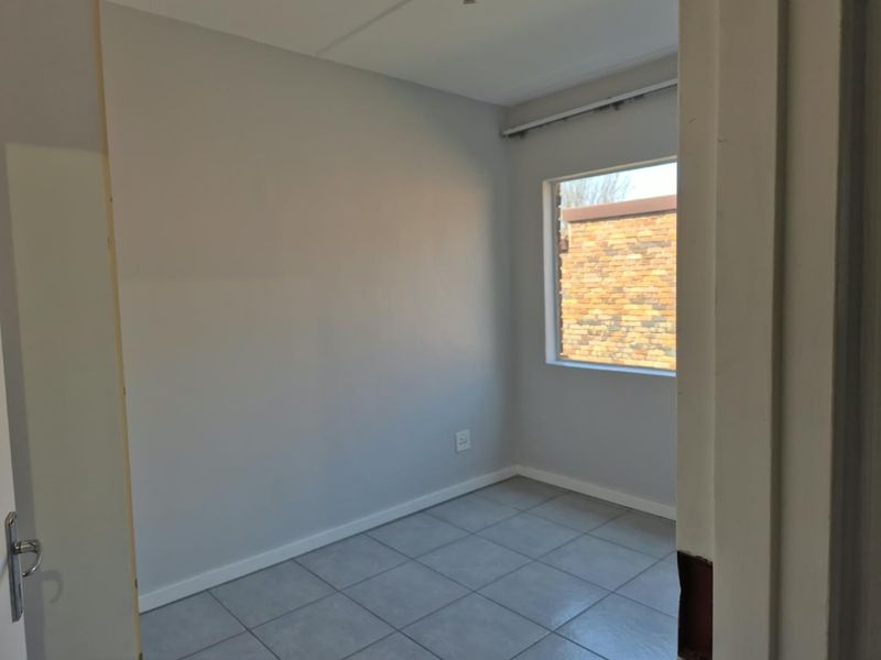 A vacant bedroom featuring neutral grey walls, tiled flooring, and a window with a curtain track, ready for personalization.