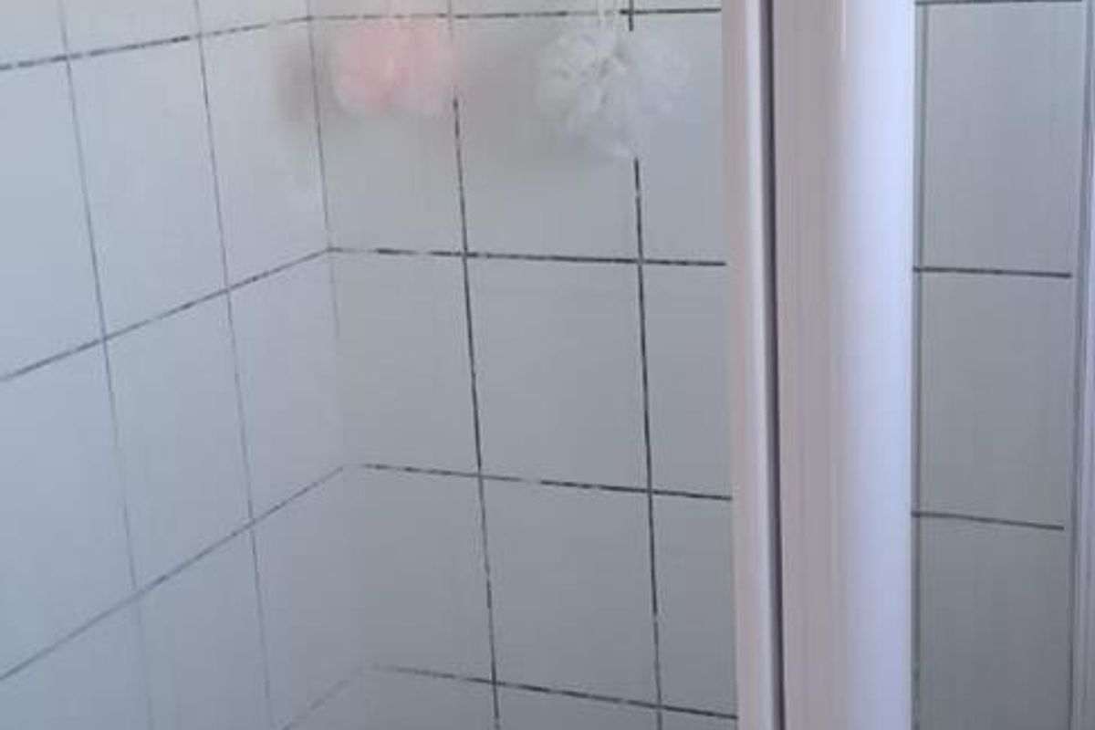 A compact shower stall featuring white wall tiles and a glass enclosure, requiring some maintenance to the grout.