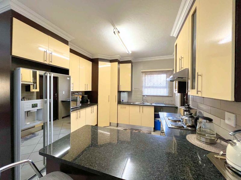 A functional kitchen featuring granite countertops, ample built-in cabinetry, a double sink, and a built-in hob with an extractor fan.