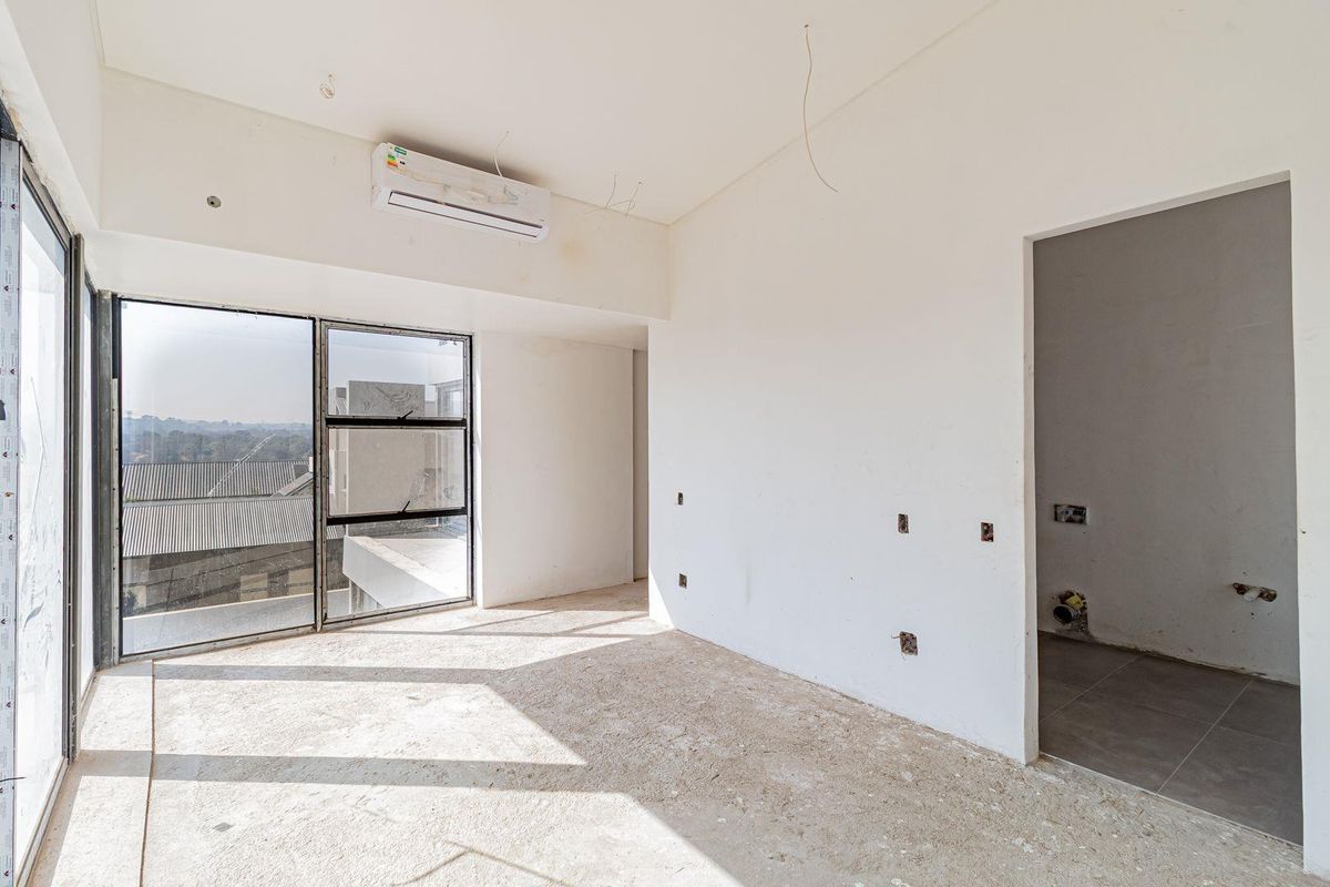 An unfinished bedroom space featuring large aluminium windows, a wall-mounted air conditioning unit, and exposed electrical points, ready for final flooring and wall finishes.