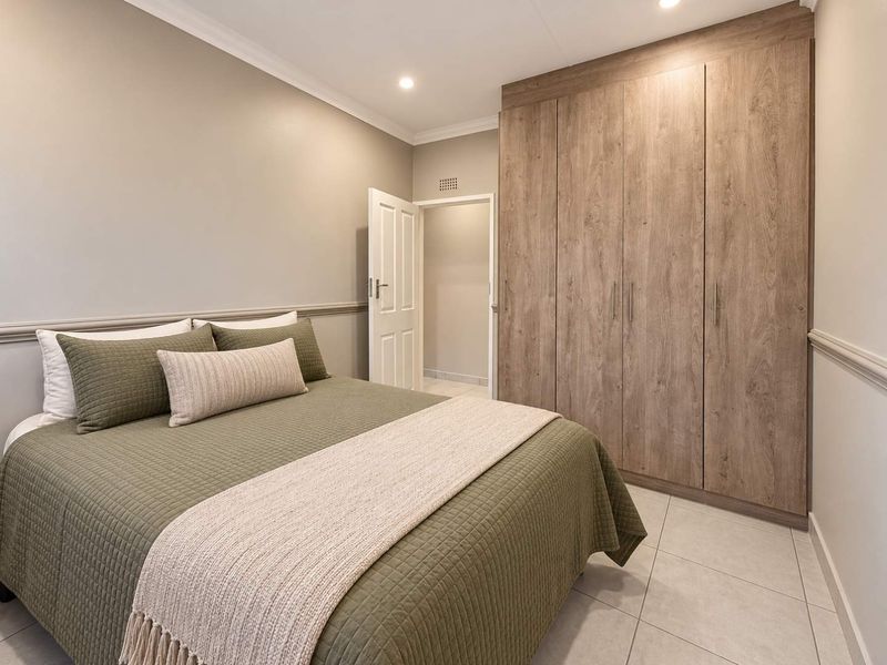 A well-maintained bedroom featuring neutral walls, tiled flooring, and ample built-in wooden cupboards, offering a clean and functional living space.
