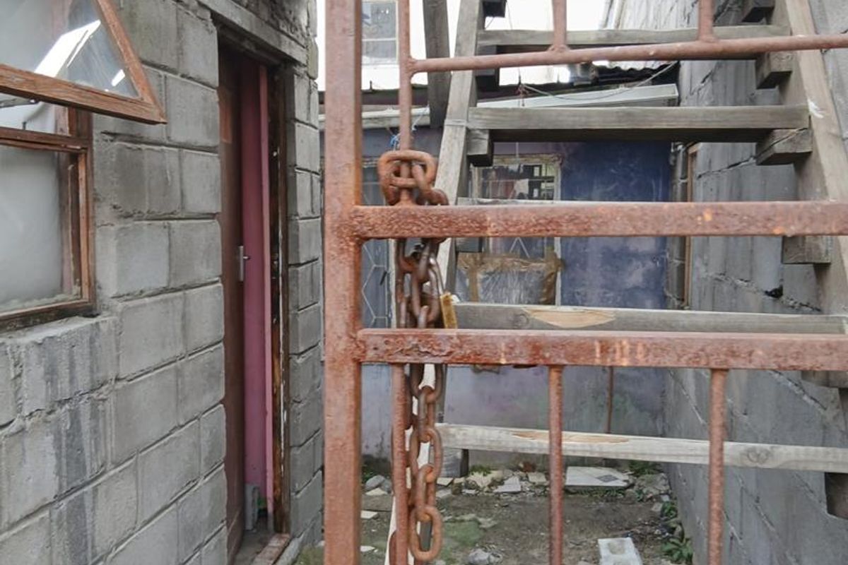 Rear exterior area featuring an external staircase, concrete block walls, and a rusted metal security gate in need of significant maintenance.
