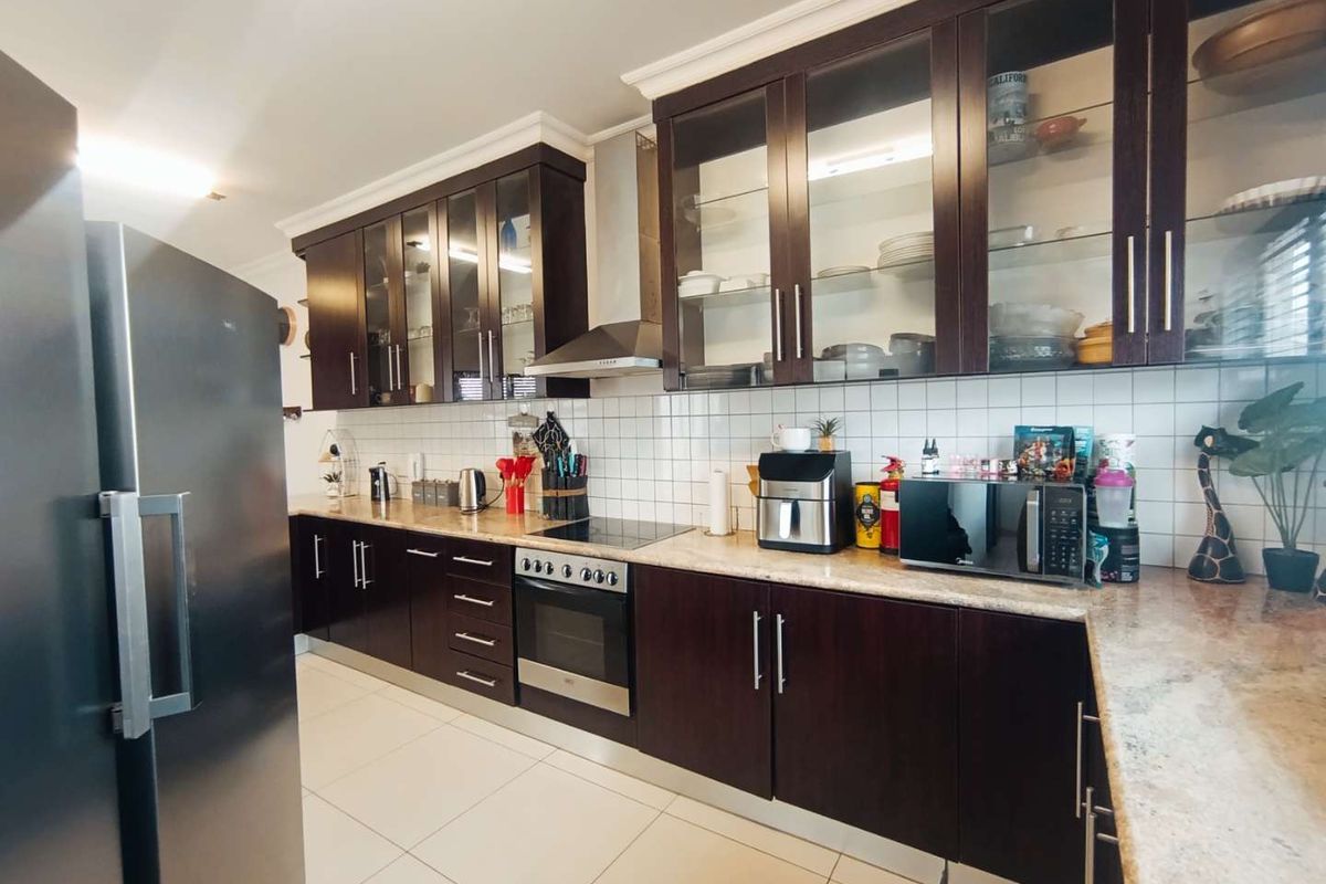 A well-maintained kitchen featuring dark wood cabinetry, glass-front display cabinets, a tiled backsplash, and integrated stainless steel oven and extractor fan.