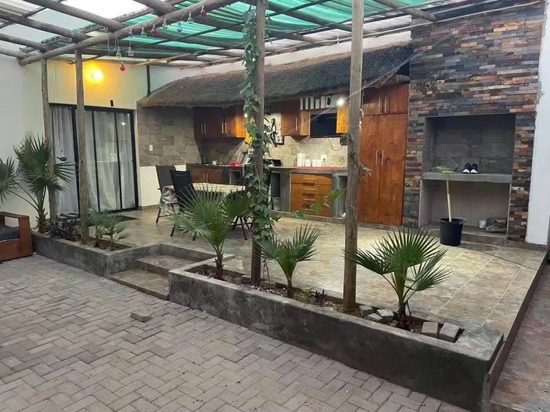Covered outdoor entertainment area featuring a built-in braai, stone cladding, timber pergola, and integrated cabinetry, perfect for alfresco dining and social gatherings.