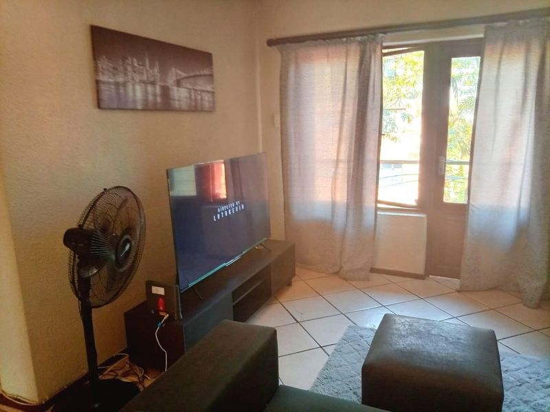 A living room area featuring tiled flooring and a glass panel door leading to an outdoor space, providing natural light to the room.