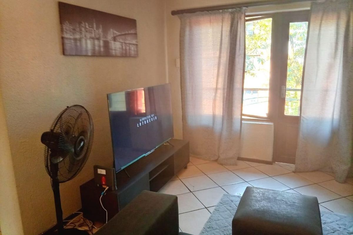 A living room area featuring tiled flooring and a glass panel door leading to an outdoor space, providing natural light to the room.