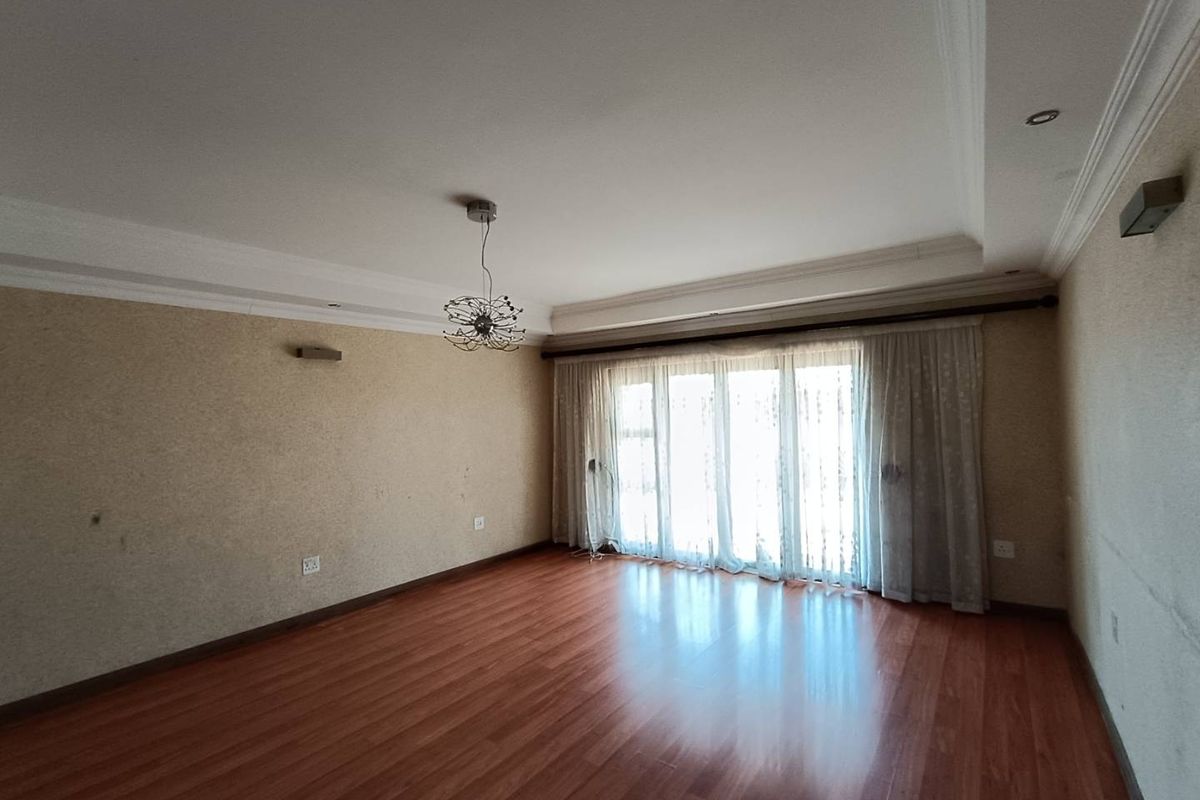 Spacious living room featuring warm-toned laminate flooring, recessed ceiling detailing, and large sliding glass doors providing ample natural light.