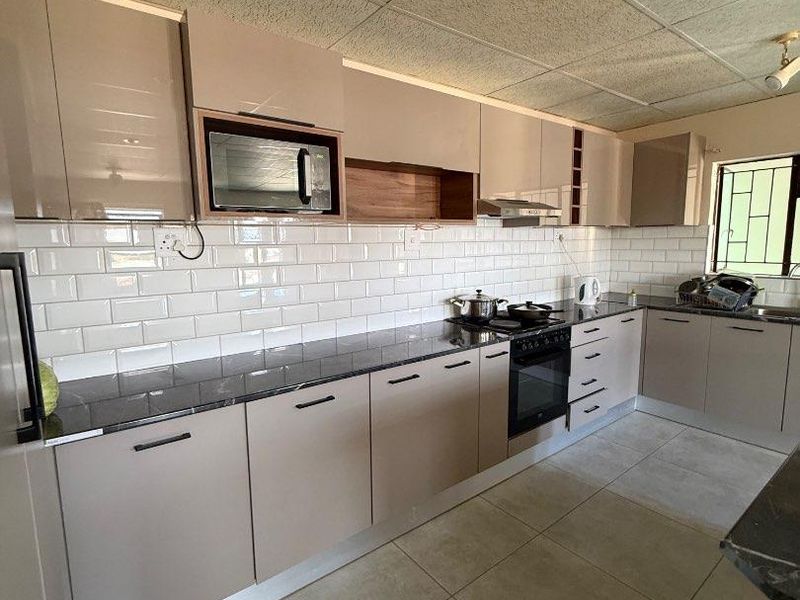Modern kitchen featuring sleek cabinetry, granite countertops, subway tile backsplash, and integrated appliances including an oven, hob, and microwave.