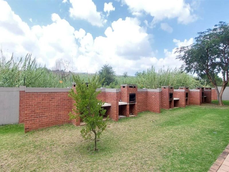 A spacious communal garden area featuring multiple built-in brick braai stations, a well-maintained lawn, and a paved walkway along the boundary wall.