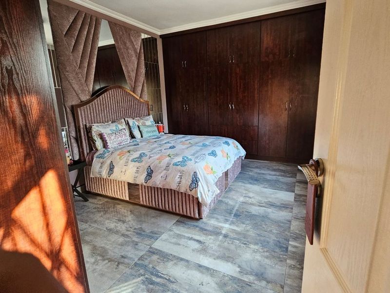 A well-maintained bedroom featuring extensive dark wood built-in cupboards, large format floor tiles, and decorative mirrored wall accents.