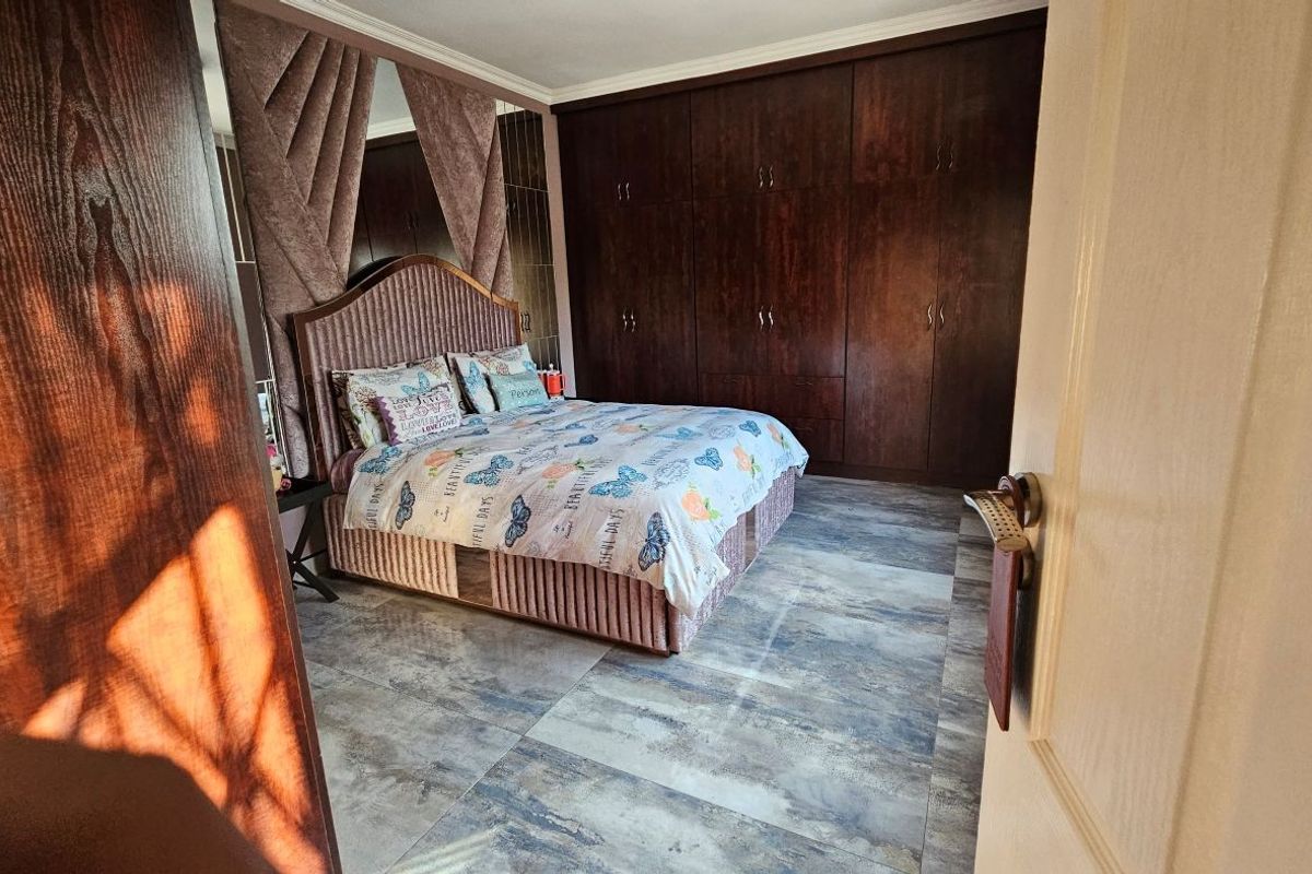 A well-maintained bedroom featuring extensive dark wood built-in cupboards, large format floor tiles, and decorative mirrored wall accents.