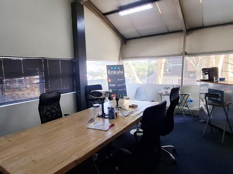 A functional office space featuring large windows, exposed roof structure, and carpeted flooring, suitable for a collaborative work environment.