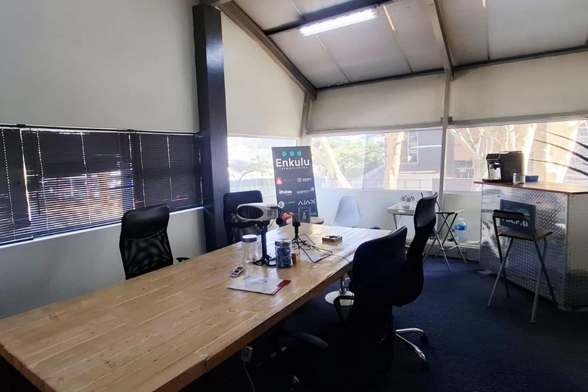 A functional office space featuring large windows, exposed roof structure, and carpeted flooring, suitable for a collaborative work environment.