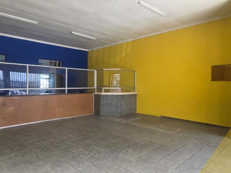 An empty commercial space featuring tiled flooring, a service counter with a glass partition, and bright yellow and blue painted walls.