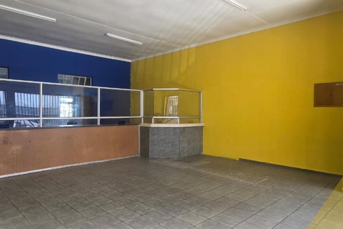 An empty commercial space featuring tiled flooring, a service counter with a glass partition, and bright yellow and blue painted walls.