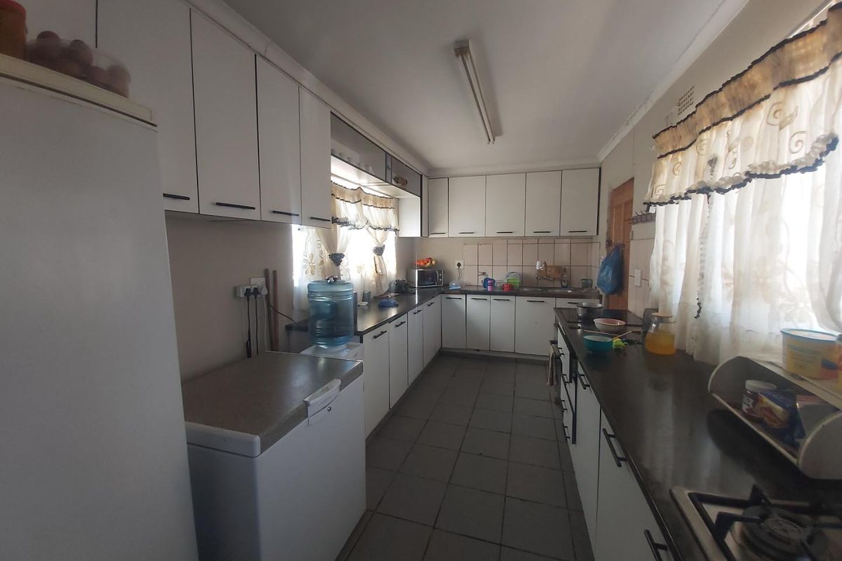 A functional kitchen featuring extensive white cabinetry, laminate countertops, tiled flooring, and a gas hob, offering a practical layout for daily meal preparation.