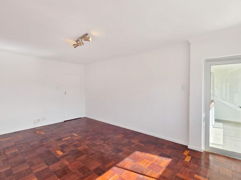 An empty living room featuring traditional parquet flooring, neutral white walls, and a glass door providing access to an outdoor area.