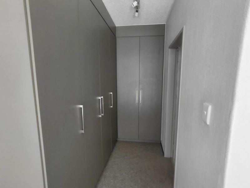 A clean hallway featuring extensive built-in cupboards with modern grey finishes and integrated storage space.