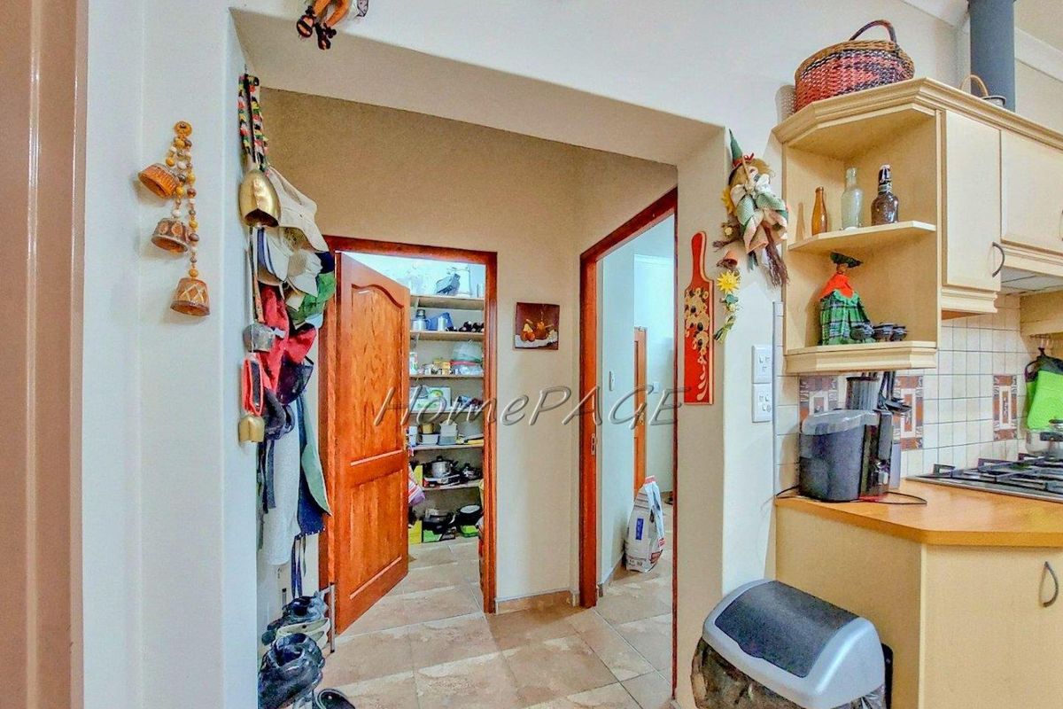 A view from the kitchen looking into a walk-in pantry and adjacent hallway, featuring tiled flooring and built-in cabinetry.