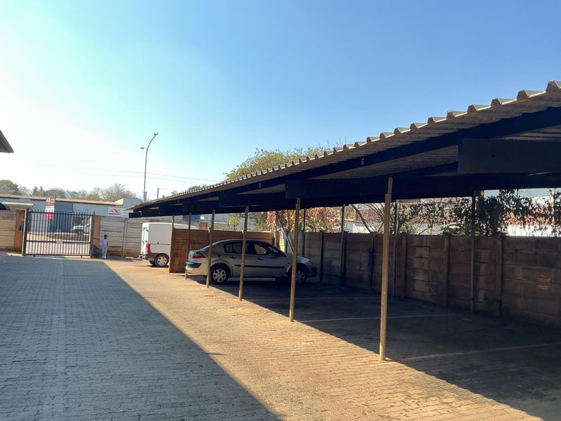 A functional outdoor covered parking area featuring multiple bays with corrugated roofing and paved surfacing, enclosed by a perimeter wall and security gate.