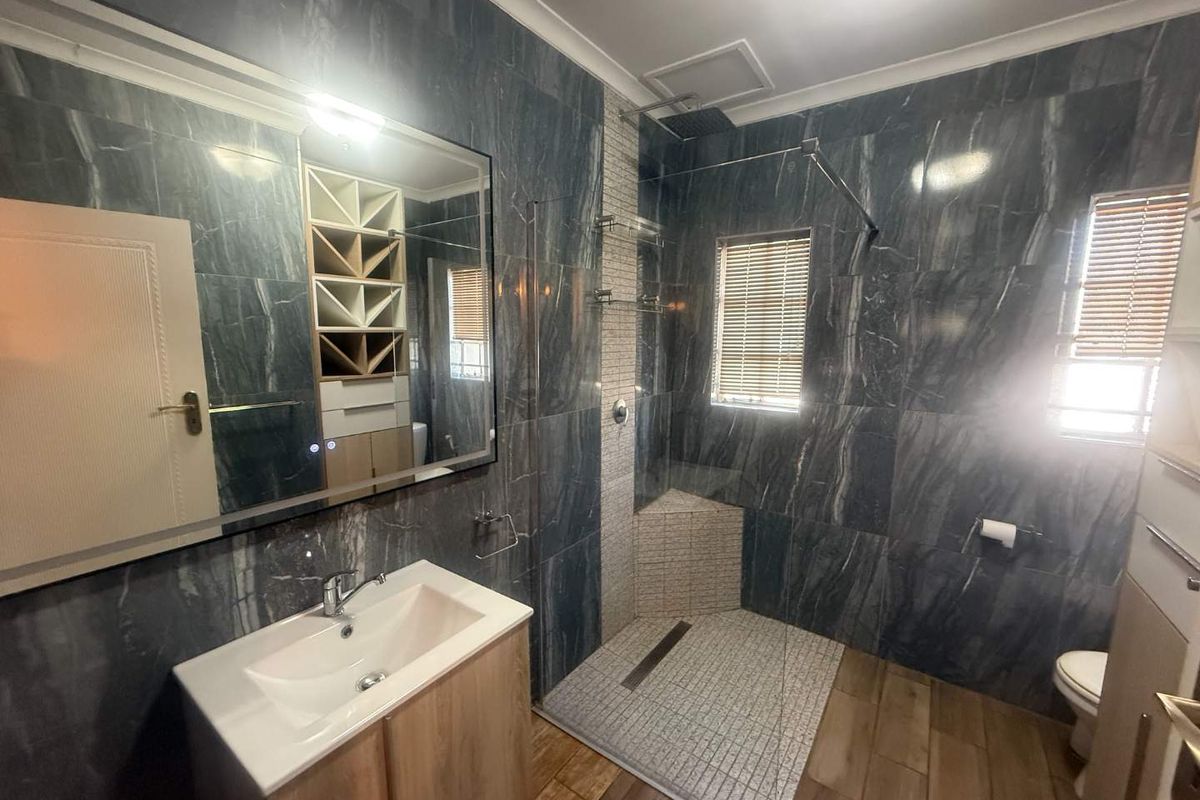 Modern bathroom featuring dark marble-look wall tiles, a spacious walk-in shower with a mosaic tiled floor, a vanity basin, and built-in storage shelving.