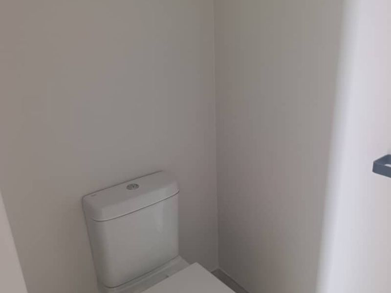 A compact, minimalist guest toilet featuring modern white sanitaryware and neutral tiled flooring.